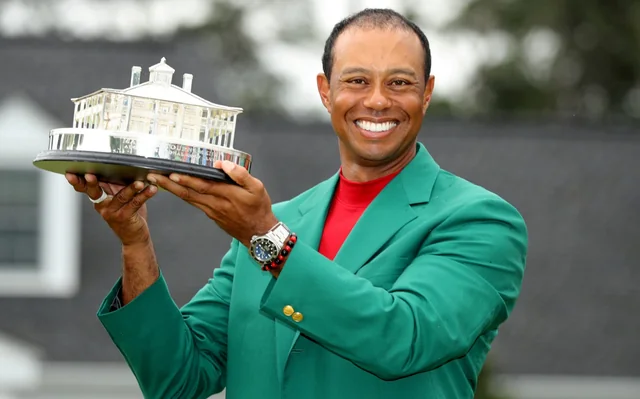 Tiger Woods smiling proudly while holding the Masters trophy, wearing the iconic green jacket after his 2019 victory.